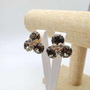 May include: A pair of gold tone clip-on earrings with three dark green and clear rhinestones each.