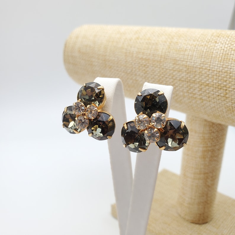 May include: A pair of gold tone clip-on earrings with three dark green and clear rhinestones each.