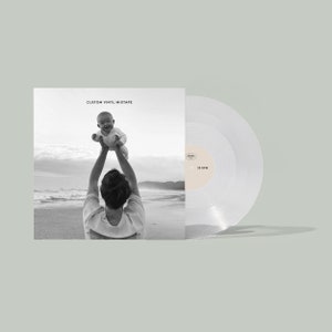 May include: A custom vinyl mixtape record with a black and white photo of a person holding a baby on a beach. The record is clear with a beige label that reads "33 RPM". The album cover reads "CUSTOM VINYL MIXTAPE".