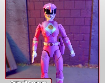 May include: A pink Power Rangers action figure from the Lightning Collection. The figure is wearing a pink suit with white and black accents, a helmet, and a belt. The figure is standing in front of a brick wall.