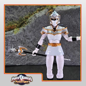 Puede incluir: Figura de acción blanca de un Power Ranger de la serie Mystic Force. La figura lleva un traje blanco y plateado con un casco y sostiene un bastón. El logotipo de Power Rangers Mystic Force está en la esquina inferior izquierda.