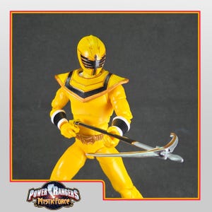 Puede incluir: Figura de acción amarilla de Power Rangers Mystic Force. La figura lleva un traje amarillo con detalles negros y un casco. Sostiene un arma plateada y negra. El logotipo de Power Rangers Mystic Force está en la esquina inferior izquierda.