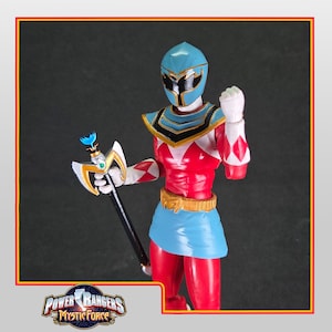 Puede incluir: Figura de acción de Power Rangers Mystic Force. La figura es predominantemente roja y azul, con detalles dorados. Sostiene un báculo con una hoja. La figura lleva un casco y una falda. El logo de Power Rangers Mystic Force está en la parte inferior.