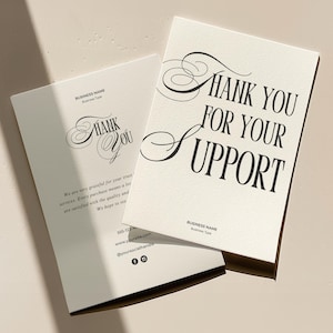 May include: A white thank you card with black text that reads "Thank You For Your Support". The card is on a light beige surface.