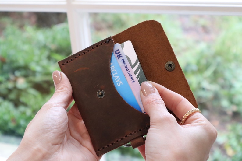 May include: A brown leather wallet with a snap closure and a card slot. The wallet is open and a UK driving licence is visible inside.