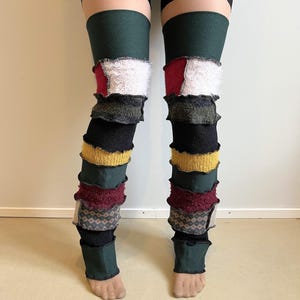 May include: Multi-colored leg warmers with a patchwork design. The leg warmers feature sections of green, white, red, black, yellow, and patterned fabrics. The leg warmers are worn from the mid-thigh to the ankles.