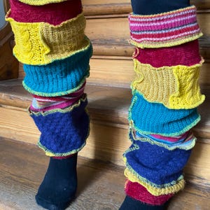 May include: A pair of colorful leg warmers in shades of yellow, red, blue, and teal. The leg warmers are made of knitted fabric and have a ruffled edge. The leg warmers are worn over black socks.