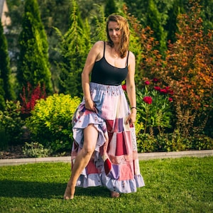 Könnte beinhalten: Eine Frau trägt ein schwarzes Tanktop und einen Patchwork-Rock mit verschiedenen Farben und Mustern. Der Rock hat einen Rüschensaum. Der Hintergrund zeigt grünes Gras, Bäume und farbenfrohes Laub.