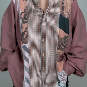 Puede incluir: Una camisa de botones de color rosa, verde y blanco con un patrón a cuadros y detalles florales. La camisa tiene mangas largas y un frente abotonado.