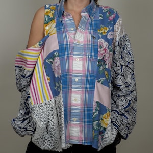 Könnte beinhalten: Ein blaues und pinkfarbenes kariertes Hemd mit floralen und gestreiften Stoffapplikationen. Das Hemd hat ein einseitiges Design und einen Spitzenbesatz.