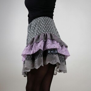 May include: A gray and black skirt with multiple layers of lace and ruffles. The skirt has a geometric pattern and a label that says "Remelin".