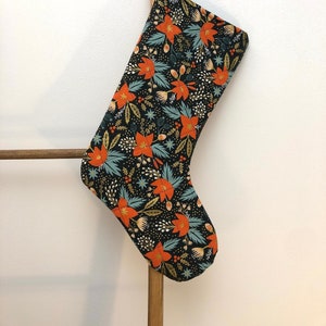 May include: A black Christmas stocking with a floral pattern featuring orange flowers, green leaves, and gold accents.