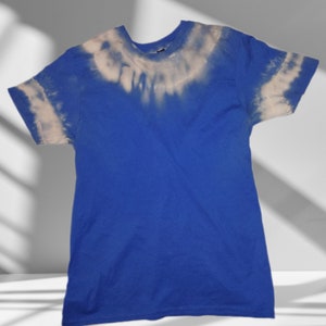 May include: A blue tie-dye t-shirt with a white bleach design. The shirt has short sleeves and a crew neck.