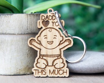 May include: Wooden keychain with a cartoon baby design. The keychain says "Daddy I love you this much" with a heart in the middle.