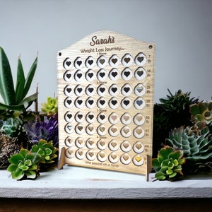 May include: A wooden weight loss tracker with a heart design. The tracker has a personalized name "Sarah's" and the text "Weight Loss Journey... one pound at a time".