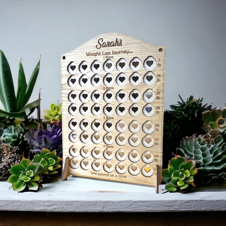 May include: A wooden weight loss tracker with a heart design. The tracker has a personalized name "Sarah's" and the text "Weight Loss Journey... one pound at a time".
