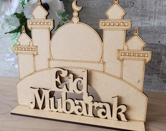 May include: Wooden cutout of a mosque with the words "Eid Mubarak" underneath. The mosque is brown and has a white dome. The words are in a white font.