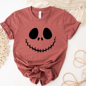 Puede incluir: Una camiseta de color marr&oacute;n rojizo con un gr&aacute;fico negro de la cara de Jack Skellington. La camiseta est&aacute; hecha de un material suave y c&oacute;modo y tiene un corte holgado.