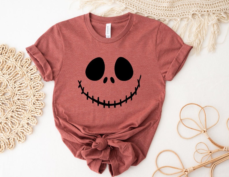 Puede incluir: Una camiseta de color marr&oacute;n rojizo con un gr&aacute;fico negro de la cara de Jack Skellington. La camiseta est&aacute; hecha de un material suave y c&oacute;modo y tiene un corte holgado.
