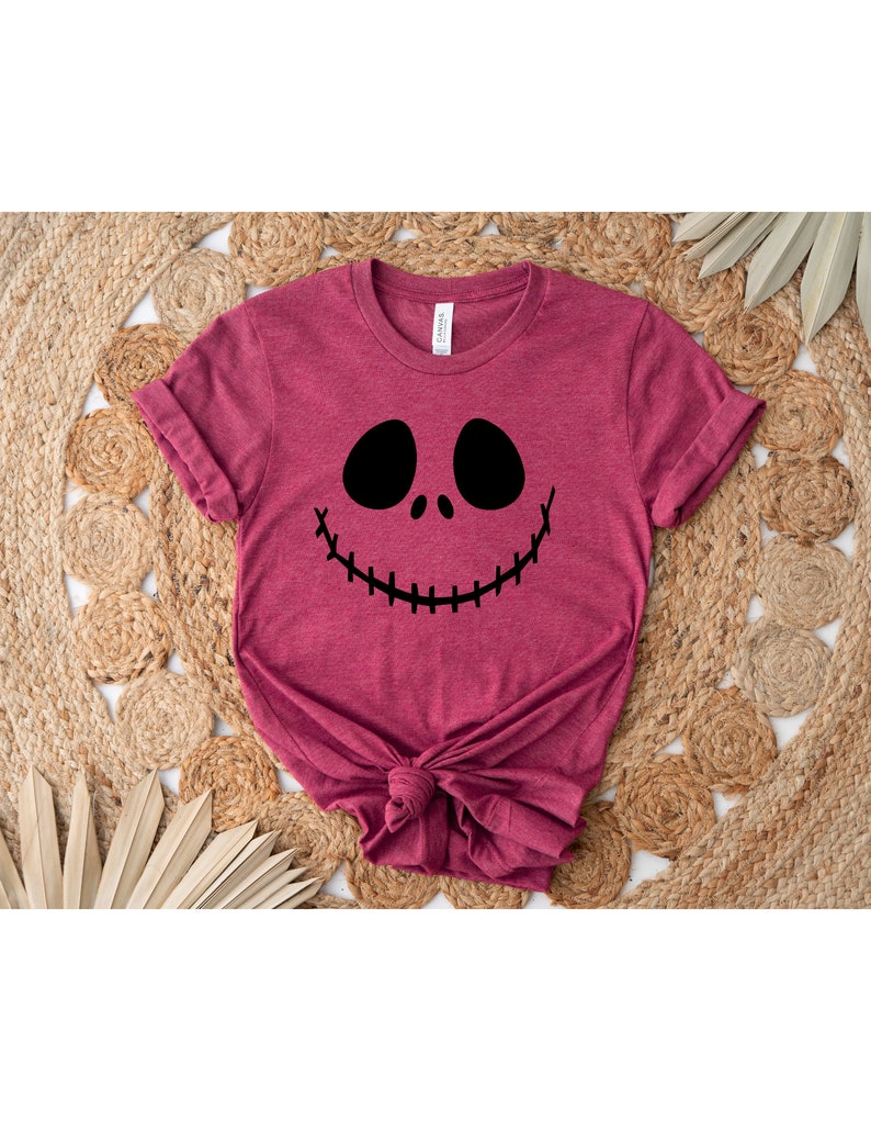 Puede incluir: Una camiseta de color granate con un gr&aacute;fico negro de la cara de Jack Skellington.