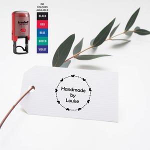 May include: A white tag with a black stamp that reads "Handmade by Louise" in a circle with a dotted line and small hearts around the edge.