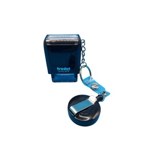 May include: Black self-inking stamp with a retractable keychain. The stamp reads "trodat printy 4910".