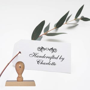 May include: A wooden stamp with a white tag that reads "Handcrafted by Charlotte" with a decorative heart and scroll design.