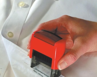 May include: A red and black self-inking stamp is pressed onto a white dress shirt. The stamp reads, "This garment belongs to Henry Johnson, Class 2B."