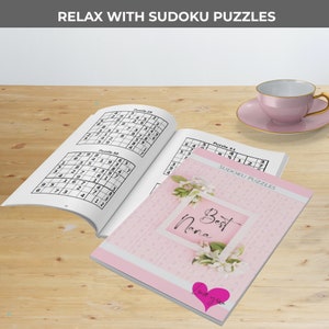 May include: A pink and white book with the words "Best Nana" on the cover. The book contains Sudoku puzzles and has a pink heart sticker with the words "Love you" on it.