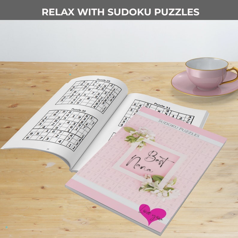 May include: A pink and white book with the words "Best Nana" on the cover. The book contains Sudoku puzzles and has a pink heart sticker with the words "Love you" on it.