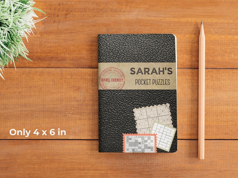 Może przedstawiać: Czarny notes w sk&oacute;rzanej oprawie z napisem "SARAH'S POCKET PUZZLES" na okładce. Notes ma wymiary 10 x 15 cm i posiada czerwoną pieczątkę "TRAVEL FRIENDLY" na okładce.