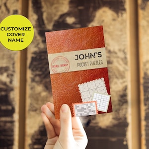 Może przedstawiać: Brązowa książka w sk&oacute;rzanej oprawie z tytułem "JOHN'S POCKET PUZZLES" i czerwoną pieczątką "TRAVEL FRIENDLY". Na okładce książki widać kilka siatek łamigł&oacute;wek.