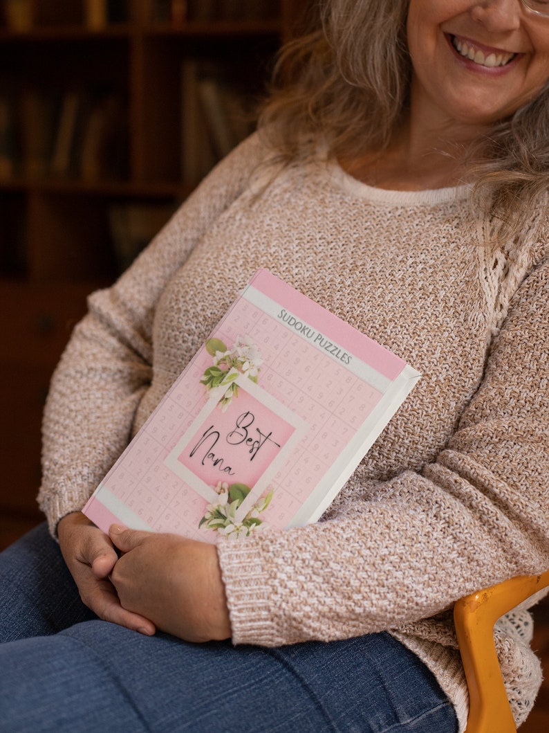 May include: A pink and white book with the text "Best Nana" and "Sudoku Puzzles" on the cover. The book is decorated with a floral design.