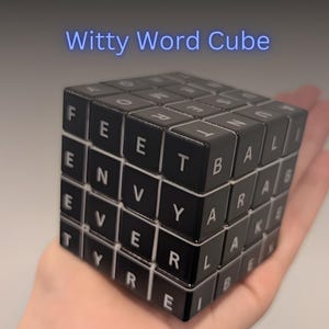 Puede incluir: Un cubo de rompecabezas negro con letras blancas en cada cara cuadrada. El texto Witty Word Cube aparece sobre el objeto. El cubo presenta varias letras dispuestas en un patrón de cuadrícula, formando palabras como FEET, ENVY, EVER, TYRE, BALI, ARAB y LAKE.