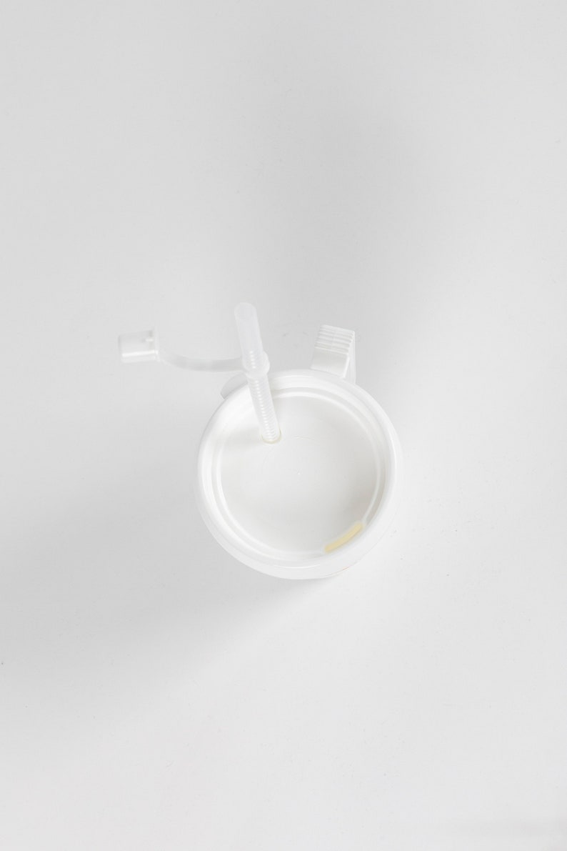 May include: White plastic cup with a lid and a straw. The lid has a small handle.