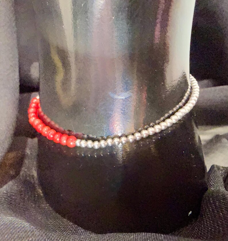 May include: A two-strand bracelet featuring red and silver beads. The red beads are a vibrant color, while the silver beads have a metallic sheen. The bracelet is displayed on a black mannequin.