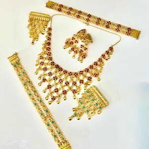 Könnte beinhalten: Ein goldfarbenes Schmuckset bestehend aus einer Halskette, zwei Armbändern und zwei Ohrringen. Die Halskette und ein Armband sind mit kleinen roten Blumenakzenten verziert. Das zweite Armband und ein Ohrring haben türkisfarbene Steine.