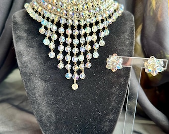 May include: A crystal choker necklace with a cascading design and matching earrings. The necklace is made of clear iridescent crystals and has a silver tone finish.