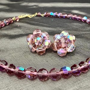 May include: A vintage jewelry set featuring a necklace and matching clip-on earrings. The set is made of faceted, iridescent purple beads with a gold-tone clasp. The earrings are clustered, and the necklace is a choker style.