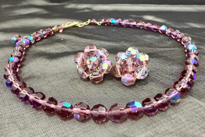 May include: A vintage jewelry set featuring a necklace and matching clip-on earrings. The set is made of faceted, iridescent purple beads with a gold-tone clasp. The earrings are clustered, and the necklace is a choker style.
