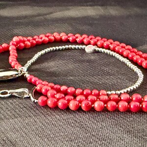 May include: A red beaded necklace with a silver clasp and a square pendant. The necklace has a double strand of small, round beads and a single strand of silver beads. The pendant is a red square set in a silver frame.