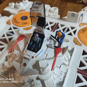 Könnte beinhalten: Ein Vintage Starcom Spielset mit einem weißen Raumschiff, Cockpit und zwei Actionfiguren. Das Set hat orangefarbene und rote Akzente, mit den Wörtern "WEIGHT" und "CAP" sichtbar. Ein Sammlerstück.