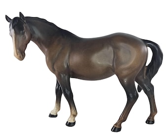 May include: A brown horse figurine with a black mane and tail. The horse has a white stripe on its face and white markings on its hooves. The figurine is standing on a white surface.