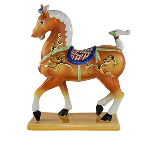 May include: A ceramic figurine of a golden horse with a blue and red saddle and a green tail. The horse is standing on a yellow base.
