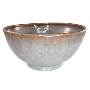 May include: A ceramic bowl with a speckled, light blue exterior and a brown rim. The bowl has a rounded shape and sits on a small, circular base. The interior is a glossy, reflective surface. This bowl is suitable for serving food.
