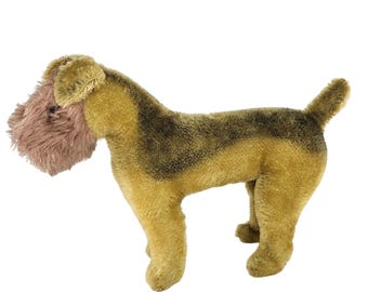 May include: A plush dog toy in shades of tan, brown, and pink. The dog has a long snout, floppy ears, and a fluffy beard. The toy is standing on all fours, with a tail pointing upwards. The dog's fur has a textured appearance.