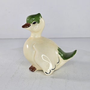 Könnte beinhalten: Eine Keramik-Entenfigur mit einem grün-weißen Bemalung. Die Ente hat einen braunen Schnabel und braune Füße.