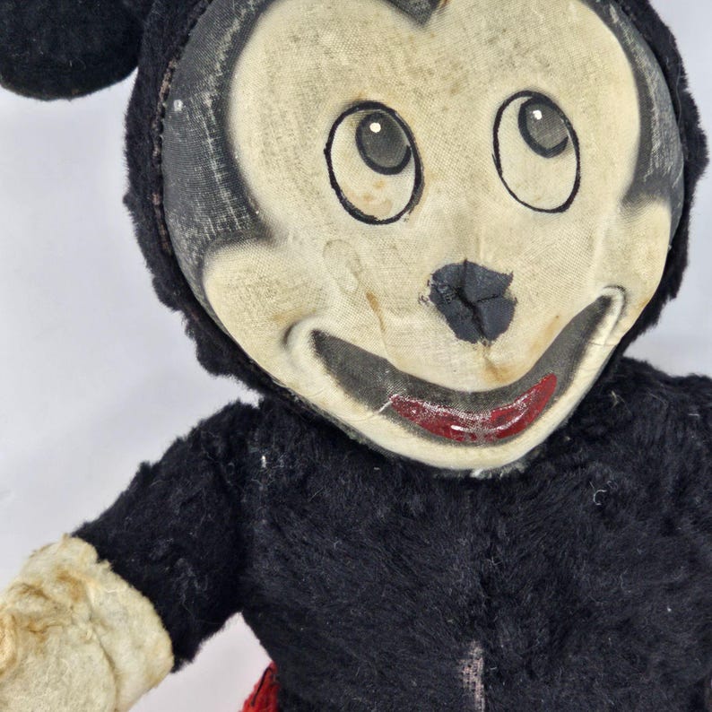 May include: Vintage Mickey Mouse plush toy with black fur, red shorts, and a white face with black eyes and a red mouth. The toy is in a worn condition, showing signs of age and use.