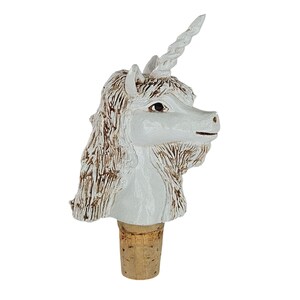 May include: A white unicorn head bottle stopper with a detailed mane and spiraled horn. The stopper is made of a light-colored material and is attached to a cork base. This decorative item is suitable for wine bottles.