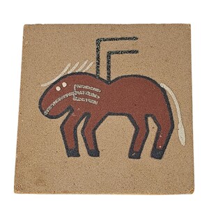 May include: Square, tan-colored tile featuring a stylized horse design. The horse is depicted in shades of brown, with white and black accents. The artwork has a textured, sandy appearance, and the horse has a unique, geometric form.